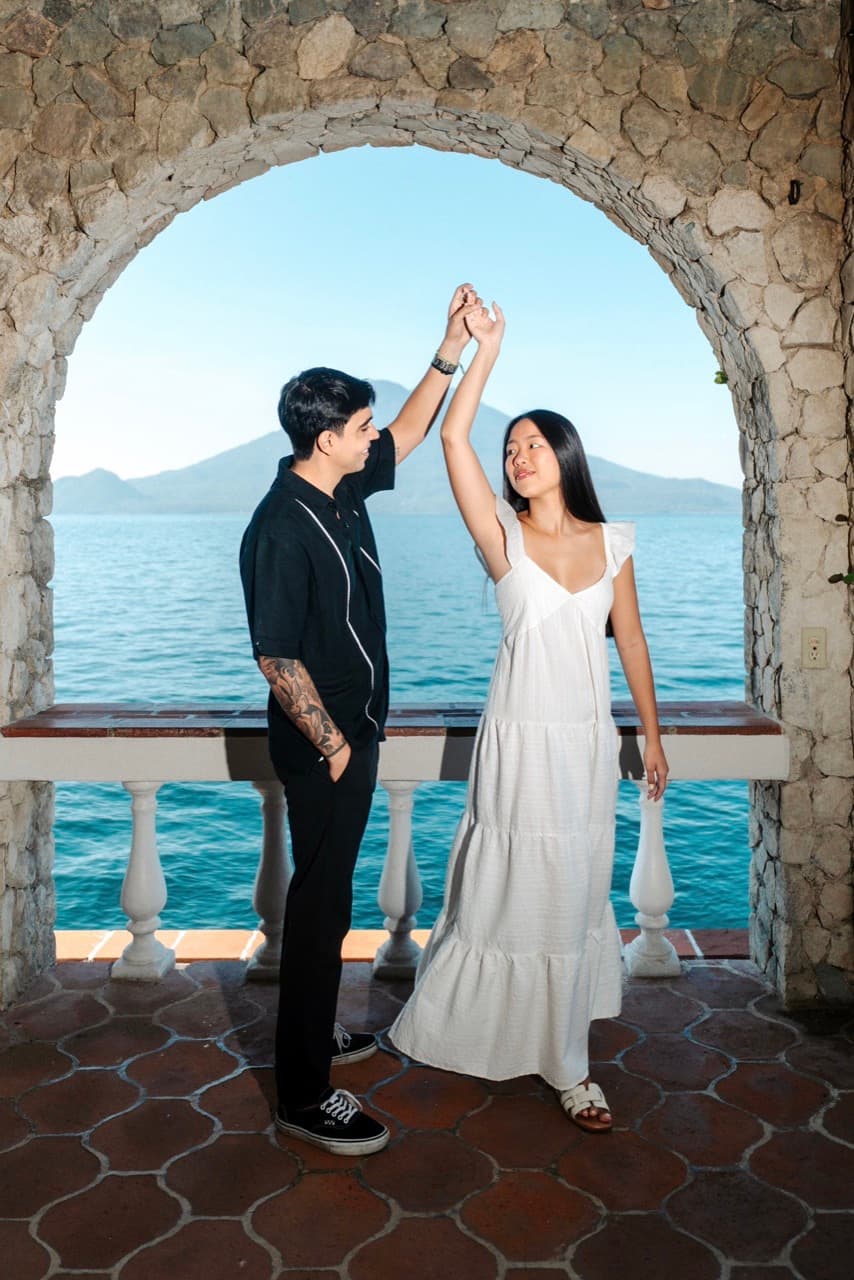 Leonardo y Emily bailando bajo un arco de piedra frente al lago